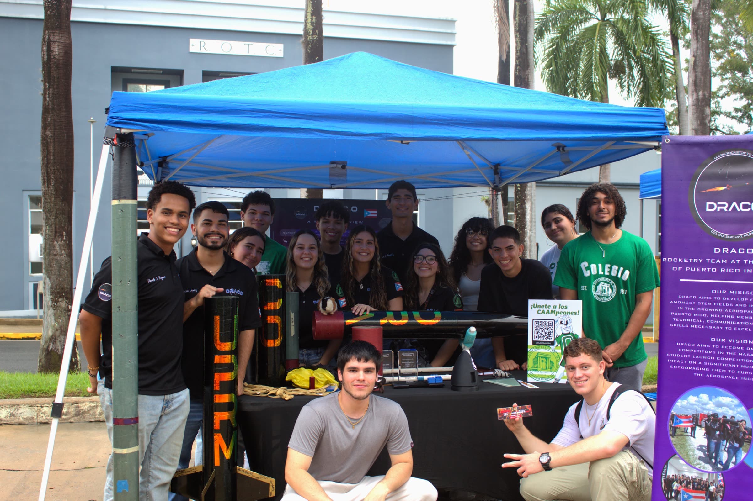 The DRACO team gathered at their booth during a UPRM campus open house, with rocket hardware and the team banner on display