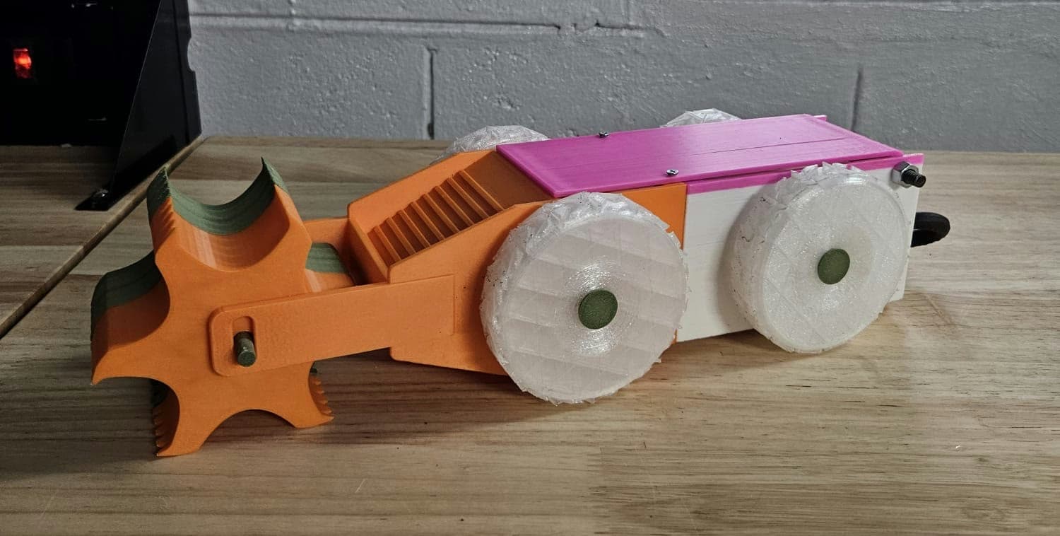 3D-printed soil-analysis rover prototype with wide white wheels and an orange front collection head, on a workbench