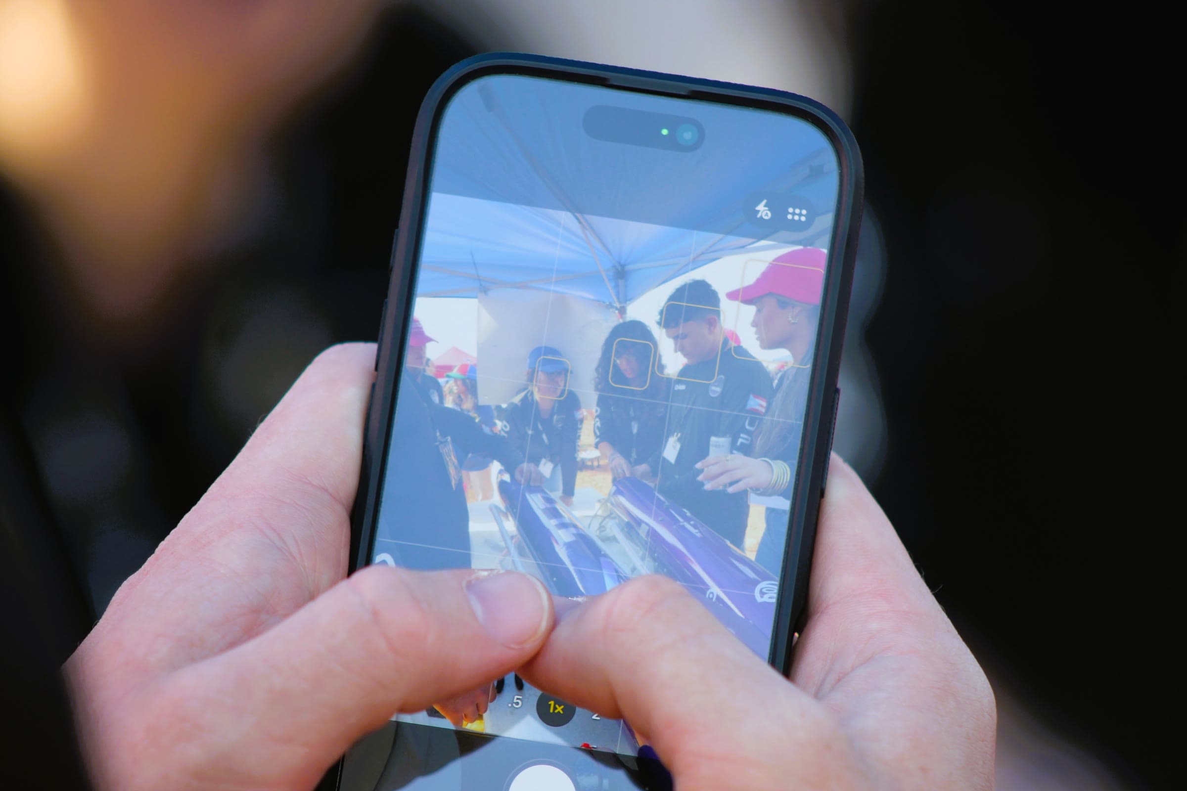 Close-up of a person's hands holding a phone, filming DRACO members working on a rocket under a tent at the competition field