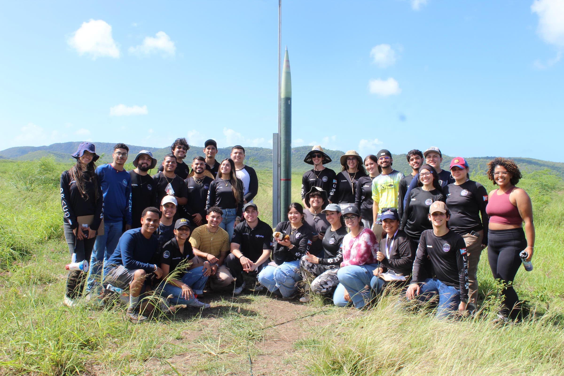 DRACO Rocketry Team posing together in the field beside a rocket on the launch rail