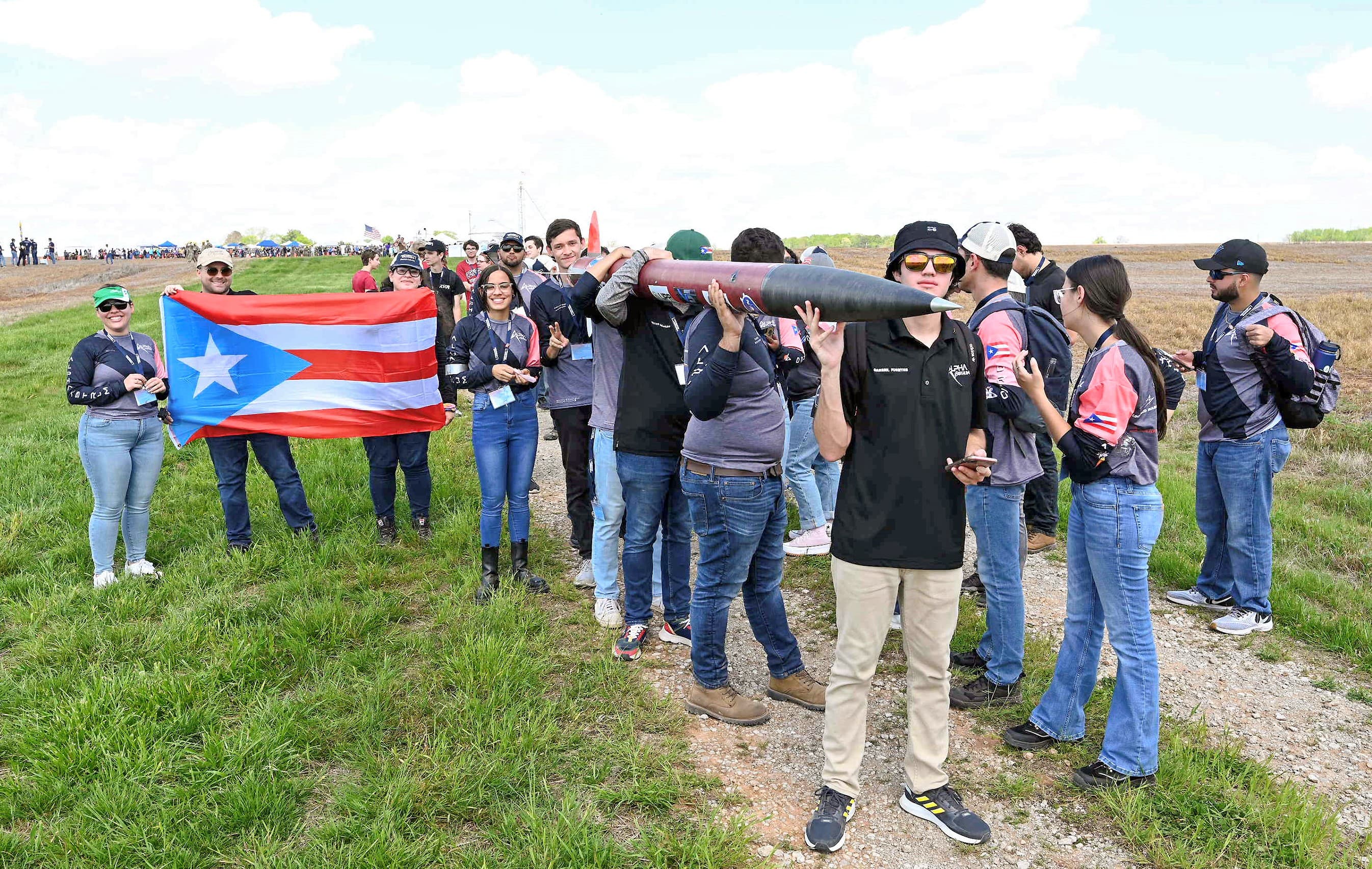 The 2023 DRACO team walking the range at competition, carrying the rocket overhead and holding a Puerto Rico flag