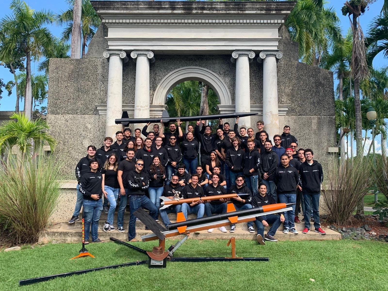 The early DRACO team posed on the steps of a monument on the UPRM campus with their rockets and launch rails laid out in front